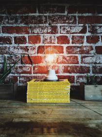 light bulb on a stack of yellow books in front of a brick wall
