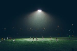 Two teams playing soccer under a big light at night