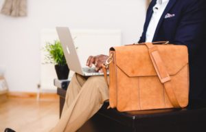 Person sitting in a suit with a briefcase and having a macbook in his lap